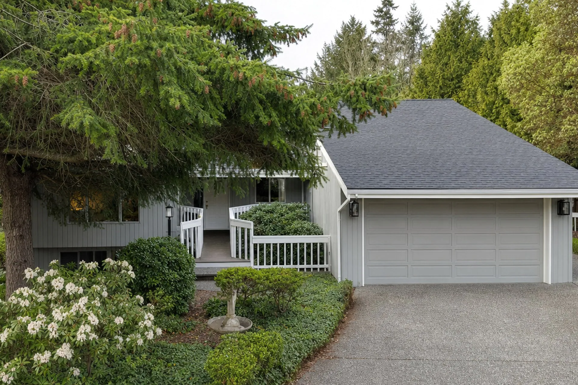 Exterior of a Pacific Northwest home with a gray two-car garage, evergreen trees and landscaped front yard before renovation